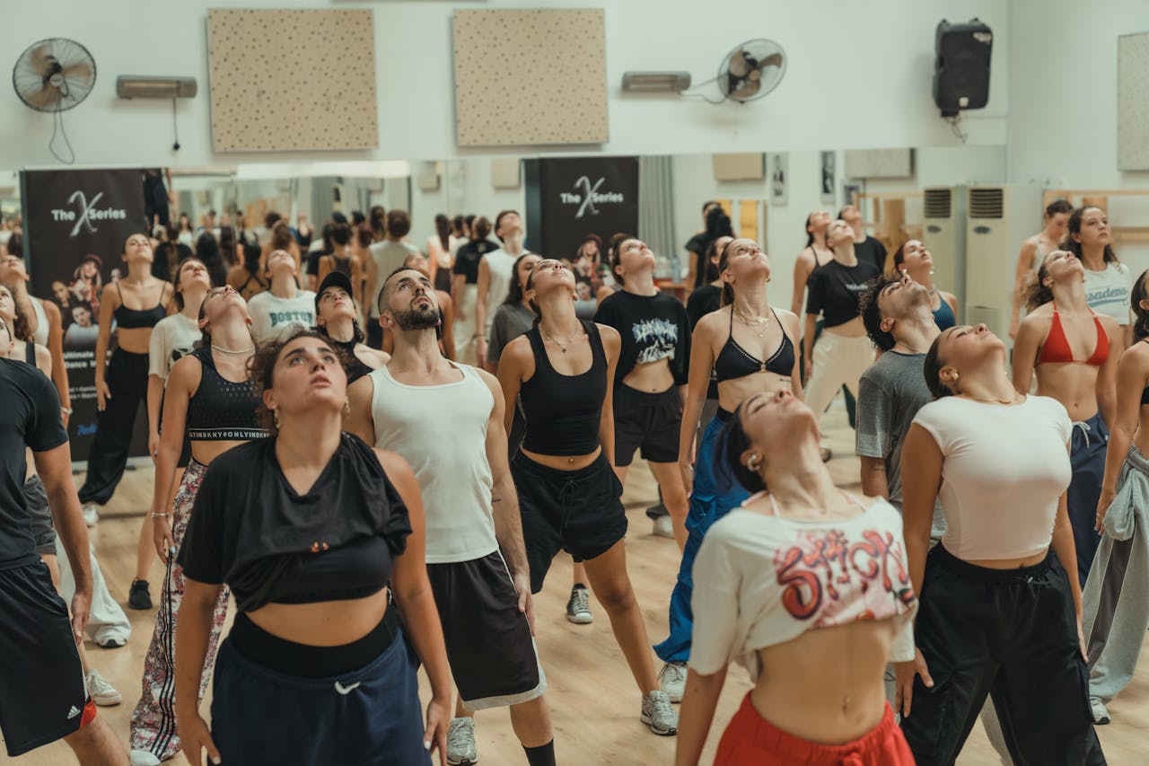 Group of men and women in a dynamic dance class indoors, emphasizing fitness and choreography.